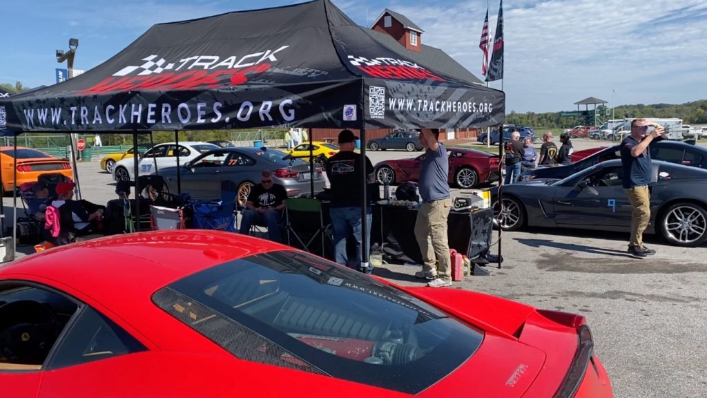 a black tent sits in the sun with track heroes.org on it, as men volunteer at an event